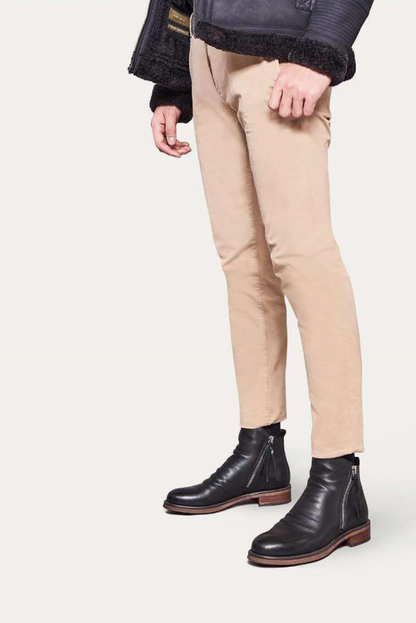 Mann in beigen Chinos, schwarzer Lederjacke und schwarzen Stiefeln mit Reißverschluss.