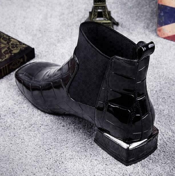 Schwarzer Stiefel von hinten seitlich mit Fersenlasche und Blockabsatz mit silberner Metallkante, auf grauem Teppich liegend. 3