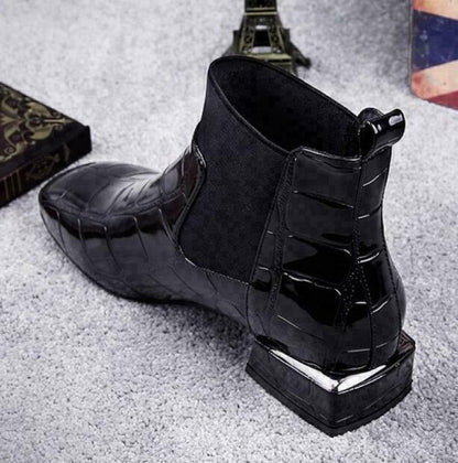 Schwarzer Stiefel von hinten seitlich mit Fersenlasche und Blockabsatz mit silberner Metallkante, auf grauem Teppich liegend. 3