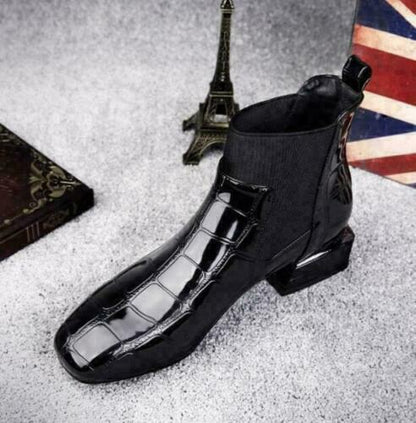 Schwarzer Krokoprägungs-Stiefel mit breitem Elastikeinsatz von schräg oben, im Hintergrund Eiffelturm-Figur und ein dunkles Buch. 5