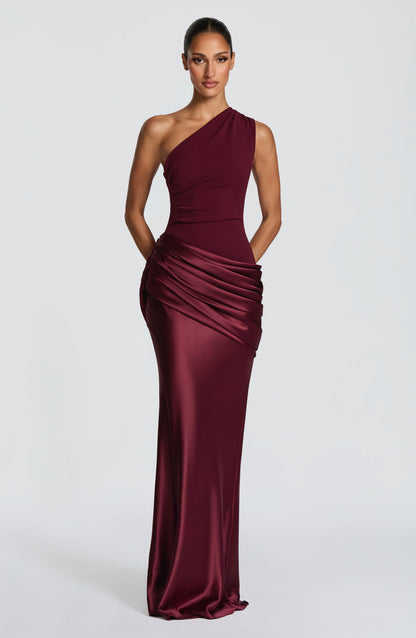Burgunderrotes One-Shoulder-Kleid in der Frontalansicht, die Hände hinter dem Rücken, mit langem, schmal fallendem Satinrock. 19