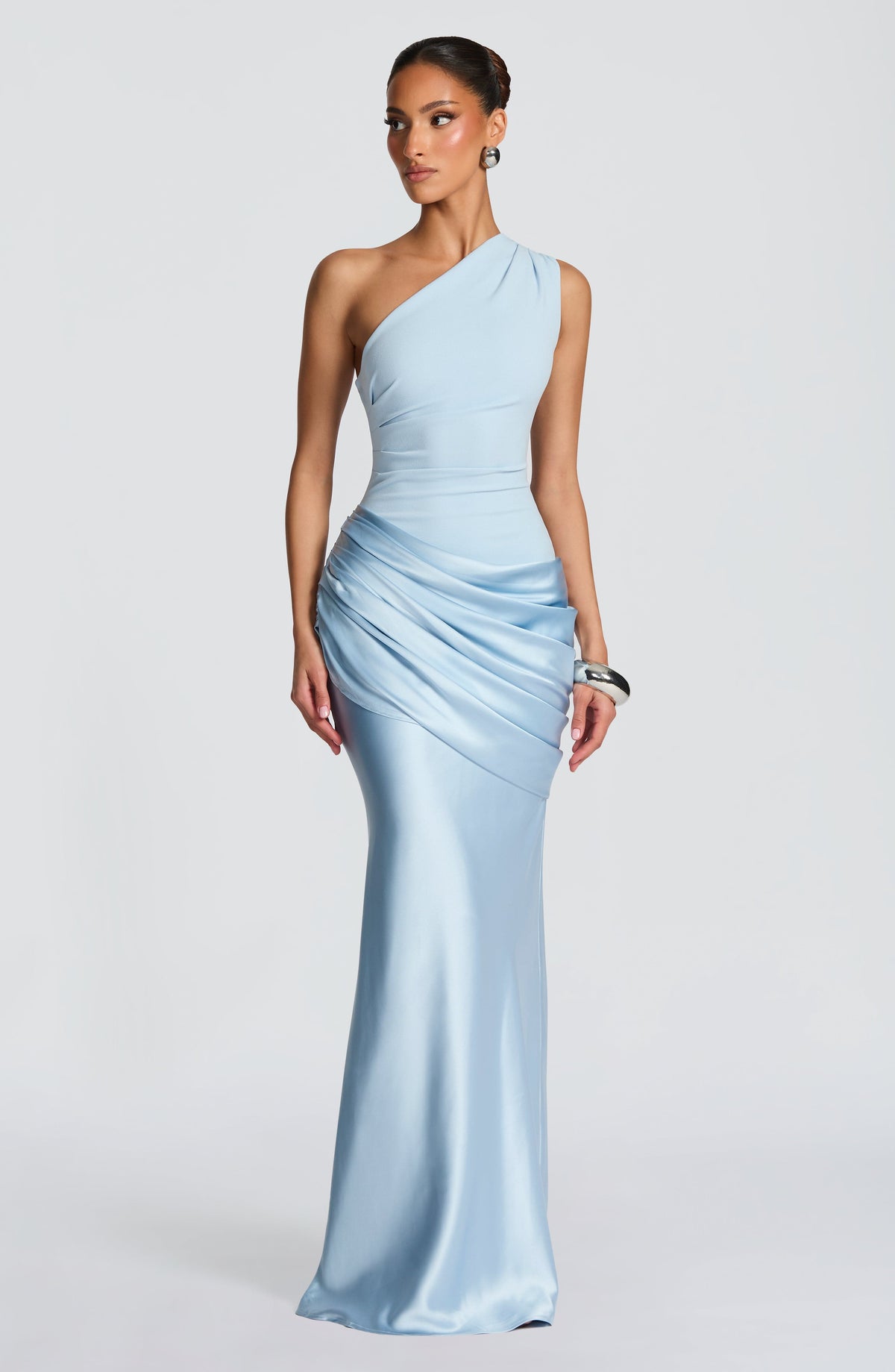 Frau in hellblauem One-Shoulder-Maxikleid mit gerafftem Satinrock, dazu silberner Ohrschmuck und ein breites silbernes Armband. 24