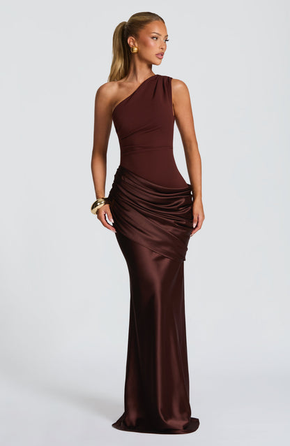 Frau mit blondem Pferdeschwanz in schokoladenbraunem One-Shoulder-Maxikleid mit glänzendem, gerafftem Satinrock, dazu goldenes Armband. 25