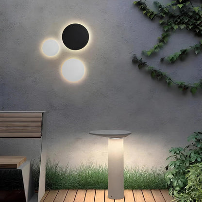 Runde Außenwandleuchte in Schwarz und Weiß mit Lichtkranz an einer Betonwand