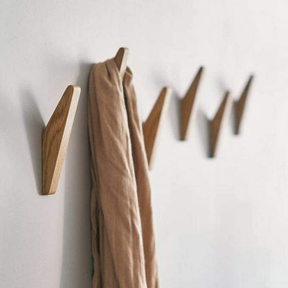 Braune Holzhaken als Detail an einer weißen Wand mit beigem Schal an einem Haken.