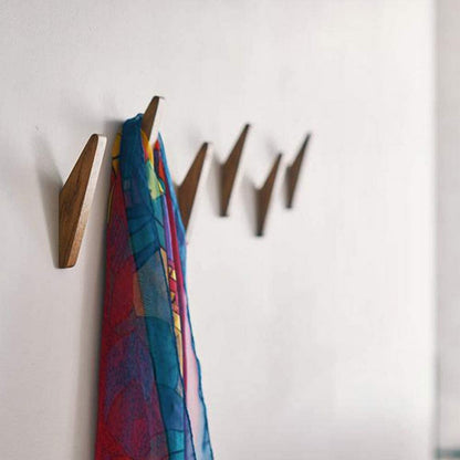 Braune Holzhaken als Detail an einer Wand mit einem bunt gemusterten Tuch.
