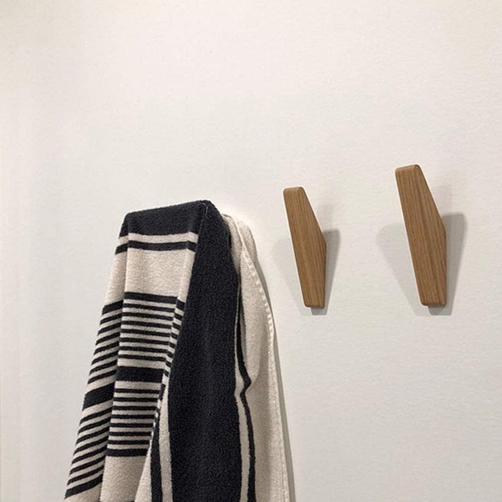Braune Holzhaken als Detail an einer weißen Wand mit schwarz-weiß gestreiftem Handtuch.
