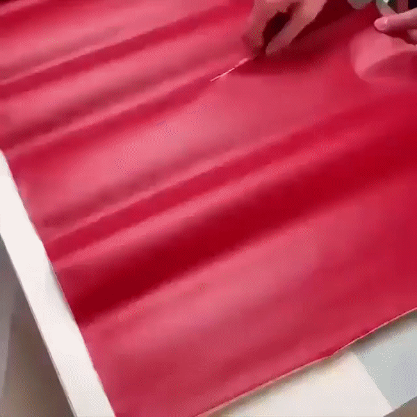 Rote Flickenbahn liegt auf einer Fläche, Hände ziehen mit einem Werkzeug eine Linie auf dem Material. 24