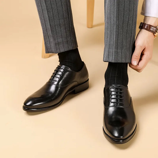 Schwarze Leder-Oxfords an den Füßen eines Mannes mit grauer Nadelstreifenhose, der den Hosensaum zurechtzieht 1