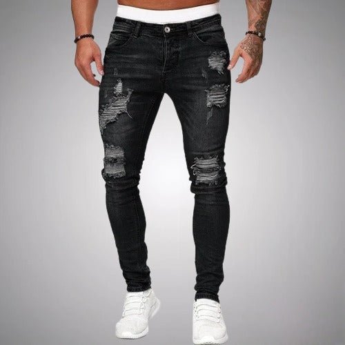 Frontansicht der eng geschnittenen, zerrissenen Jeans in Schwarz mit weißen Sneakern vor grauem Hintergrund.
