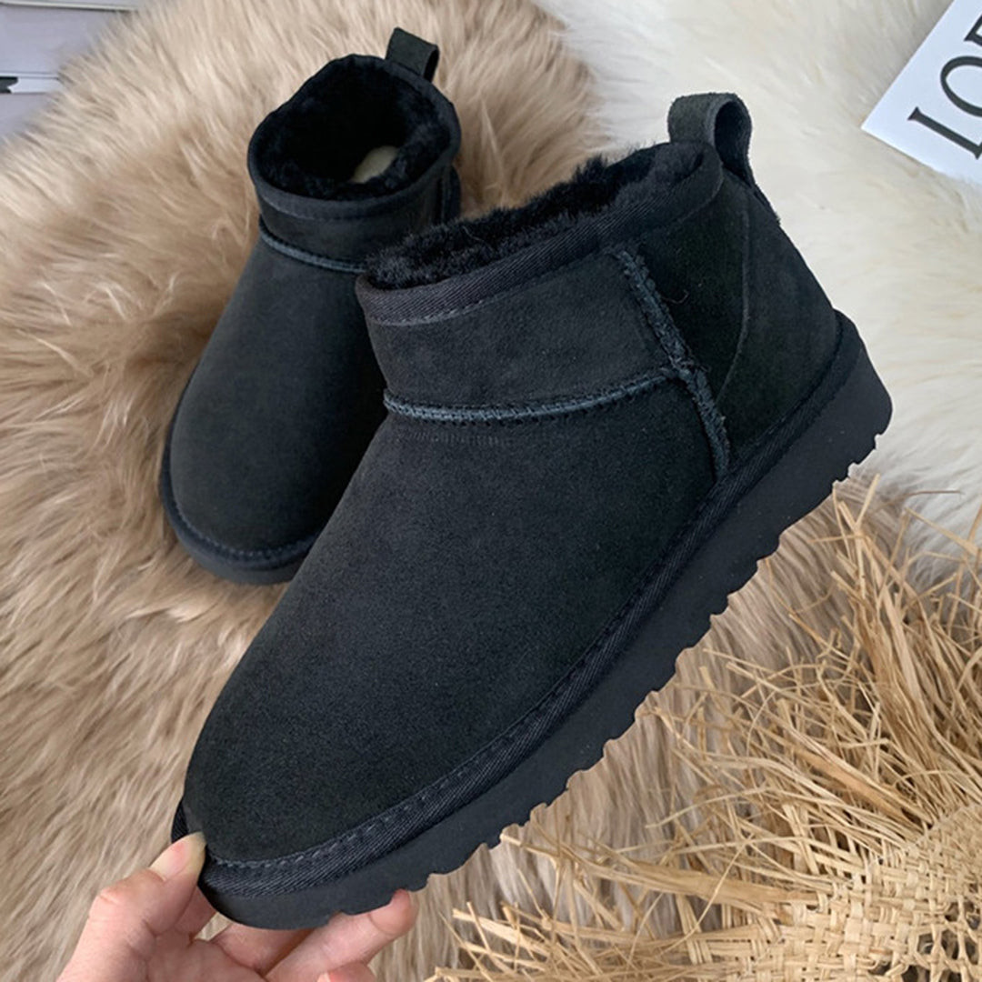 Schwarze Damen-Winterstiefel aus Wildleder mit Fellfutter auf beigem Teppich.