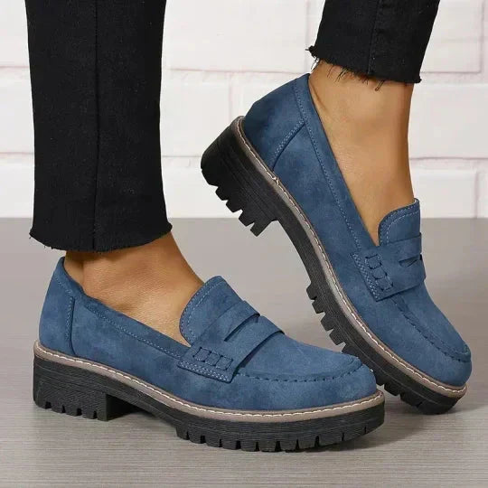 Blaue Loafer mit dicker schwarzer Sohle, getragen zu schwarzen Hosen.