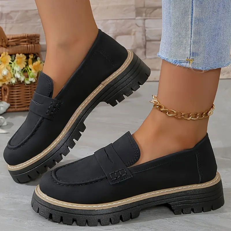 Schwarze Loafer mit heller Ziernaht an der Sohle und goldener Fußkette.