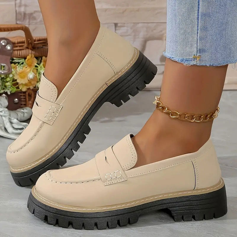 Beige Loafer mit kräftiger schwarzer Plateausohle und goldener Fußkette.