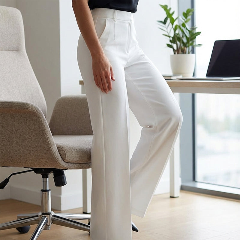 Weiße Hochtaillenhose im Detail seitlich am Model, daneben Bürostuhl, Schreibtisch mit Laptop und Zimmerpflanze.