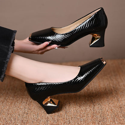 Schwarze Pumps mit Schlangenprägung, ein Schuh in der Hand gehalten, der andere getragen.