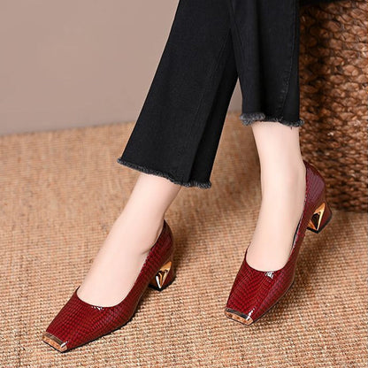 Weinrote Pumps mit Schlangenprägung und goldfarbenen Metallakzenten an Spitze und Absatz.