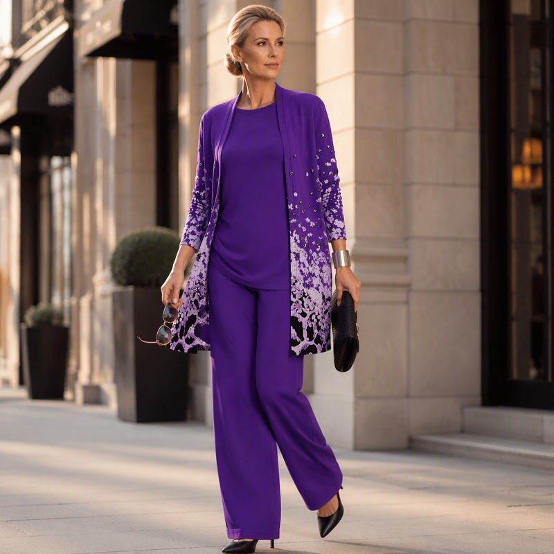 Model in violettem Set auf einer Straße, mit Sonnenbrille und schwarzer Clutch in der Hand, schwarze spitze Pumps dazu. 12