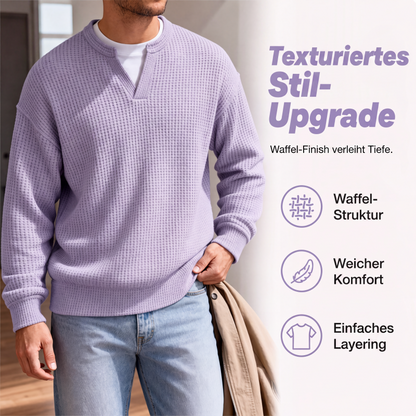 Nahaufnahme des fliederfarbenen Waffelstrick-Oberteils mit V-Ausschnitt, getragen mit heller Jeans und einer beigen Jacke über dem Arm. 3