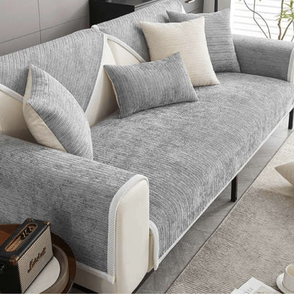 Grauer gerippter Sofaschutz auf einem Sofa mit grauen und beige Kissen.