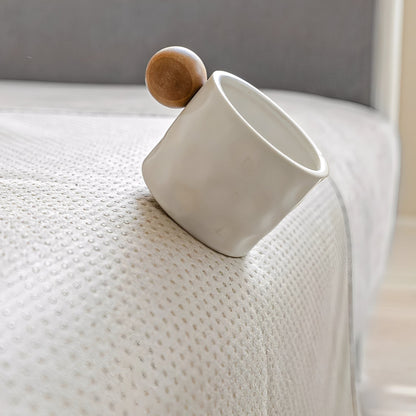 Weiße Tasse mit Holzkugel auf der Ecke eines Sofas mit rutschhemmender Noppenrückseite.