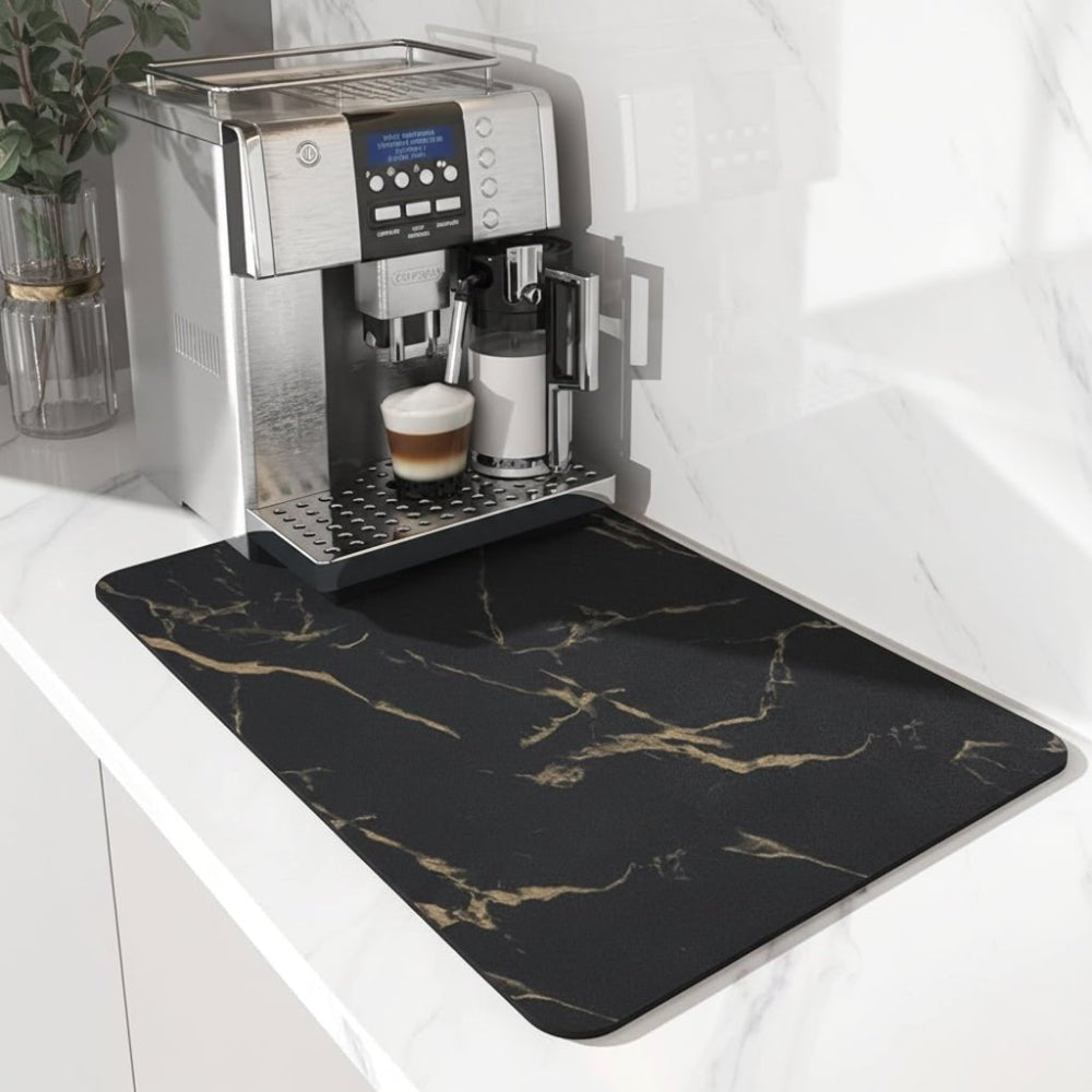 Schwarze Unterlage mit goldfarbener Marmoradern vor einem Kaffeevollautomaten auf heller Marmor-Arbeitsplatte, links eine Pflanze in Glasvase. 5