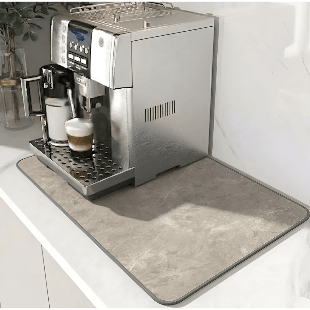 Beige Unterlage mit Steinmusterung und grauem Rand unter einem Kaffeevollautomaten, der einen Milchkaffee zubereitet, auf weißer Arbeitsplatte. 11