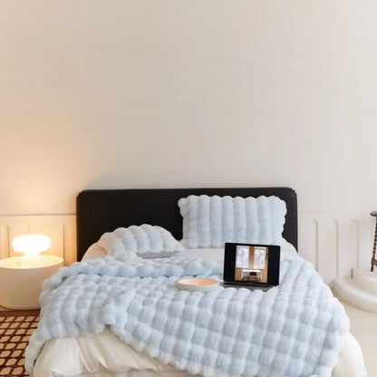Bett mit hellblauer Noppen-Plüschdecke und passenden Kissen, darauf Laptop und Kerzenschale, Lampe links 5