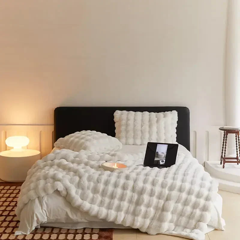 Bett mit cremeweißer Noppen-Plüschdecke und Kissen, darauf Laptop und Kerze, im hellen Schlafzimmer 6
