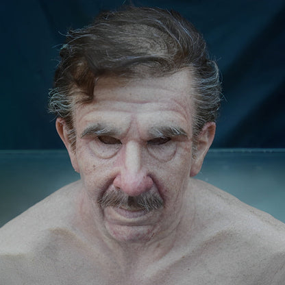 Realistische Gesichtsmaske eines älteren Mannes mit zurückgekämmtem braun-grauem Haar, Schnurrbart und Falten.