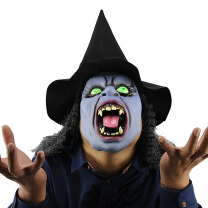 Hexenmaske mit blassblauem Gesicht, grünen Augen, aufgerissenem Mund mit Fangzähnen, schwarzem Spitzhut und dunklem Lockenhaar, getragen mit erhobenen Händen. 22