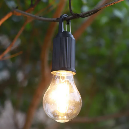 Warm leuchtende Birnenlampe mit schwarzem Haken hängt an einem Ast vor grünem, unscharfem Garten 10