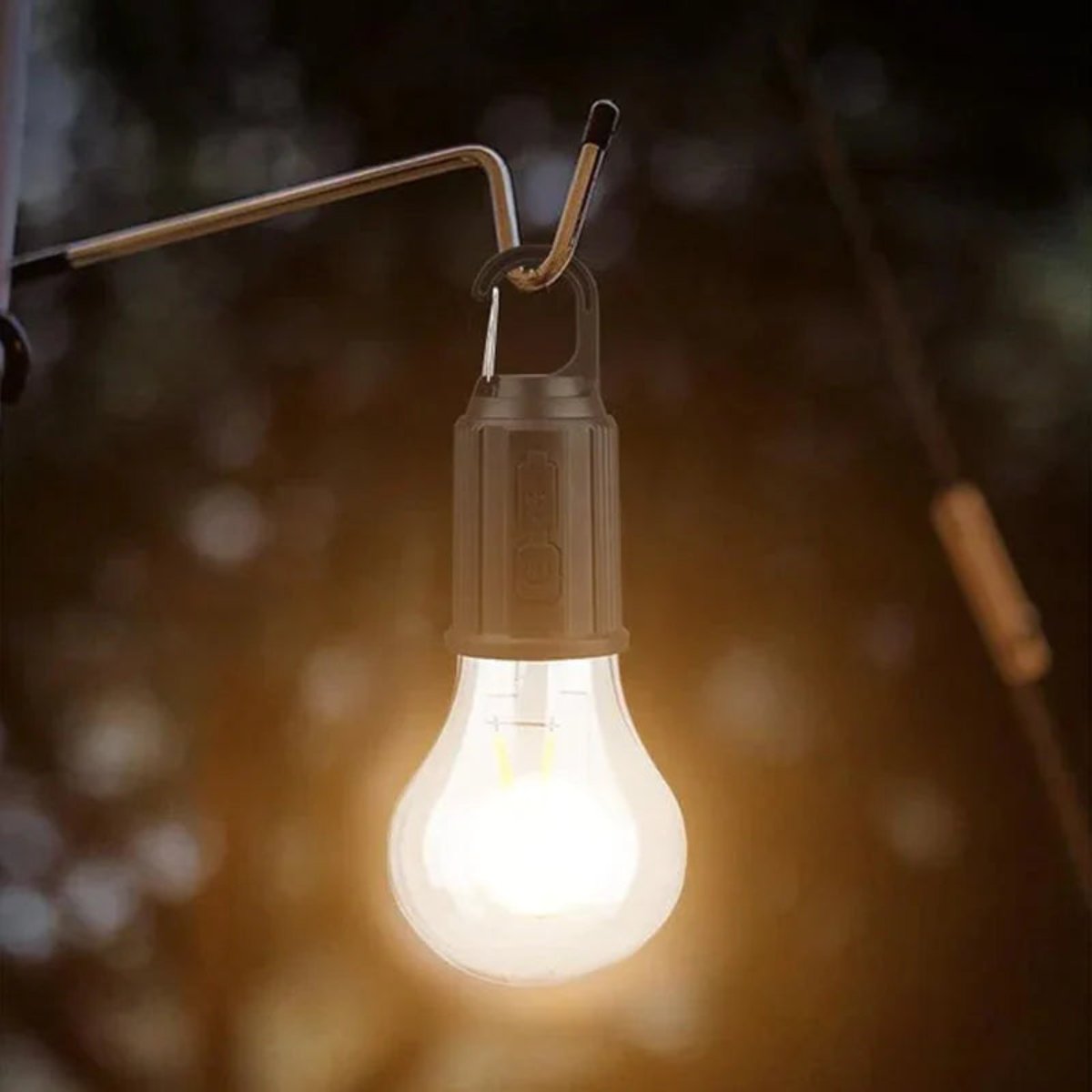 Warm leuchtende Birnenlampe hängt mit Karabiner an einem Metallhaken, Hintergrund bei Dämmerung unscharf 4