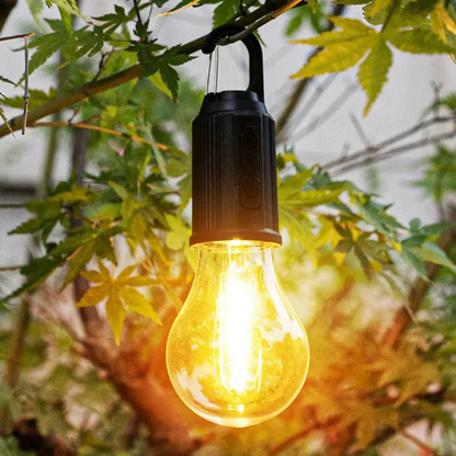 Leuchtende Glühbirnenlampe hängt an einem Zweig zwischen grünen Ahornblättern im Freien 8