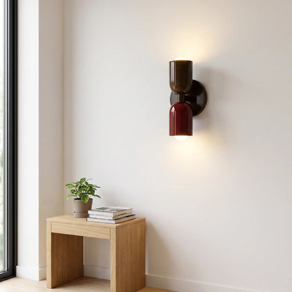 Wandlampe in Braun und Burgunderrot mit zwei leuchtenden Kugellampen an heller Wand über einem Holzhocker mit Pflanze und Büchern. 10