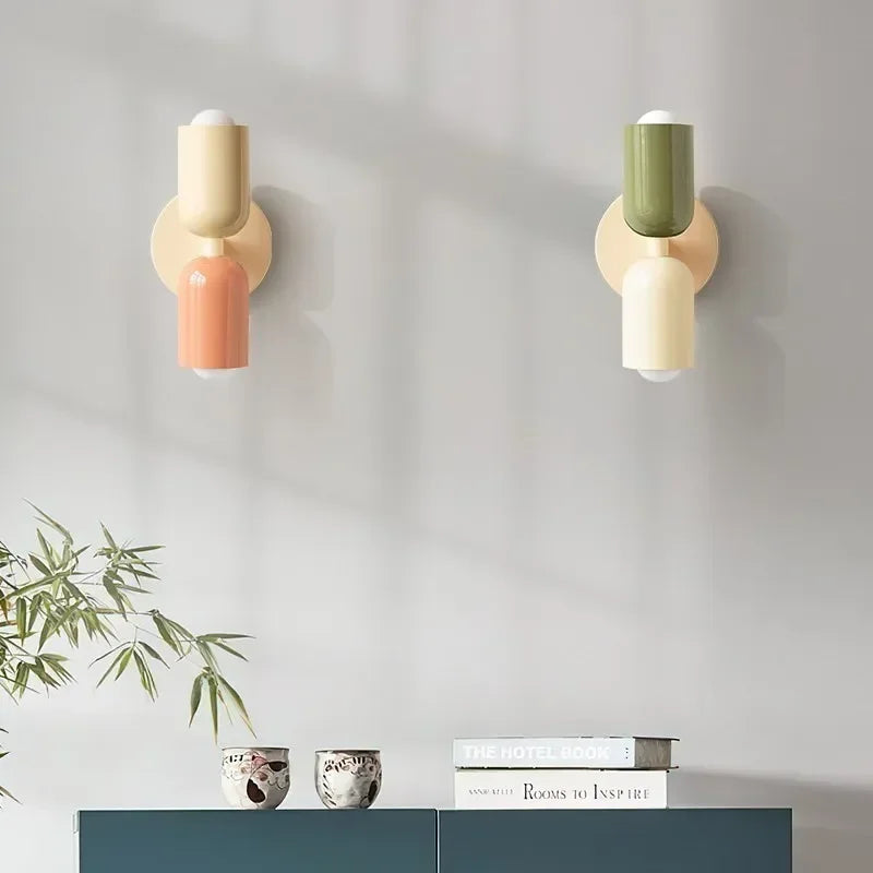 Zwei Wandlampen, eine in Creme-Lachs und eine in Grün-Creme, über einem blaugrünen Sideboard mit Büchern, Schälchen und Bambuszweigen. 14