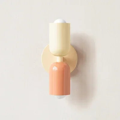 Einzelansicht der Wandlampe mit cremefarbenem Oberteil, lachsfarbenem Unterteil und cremefarbenem Wandteller vor heller Wand. 16