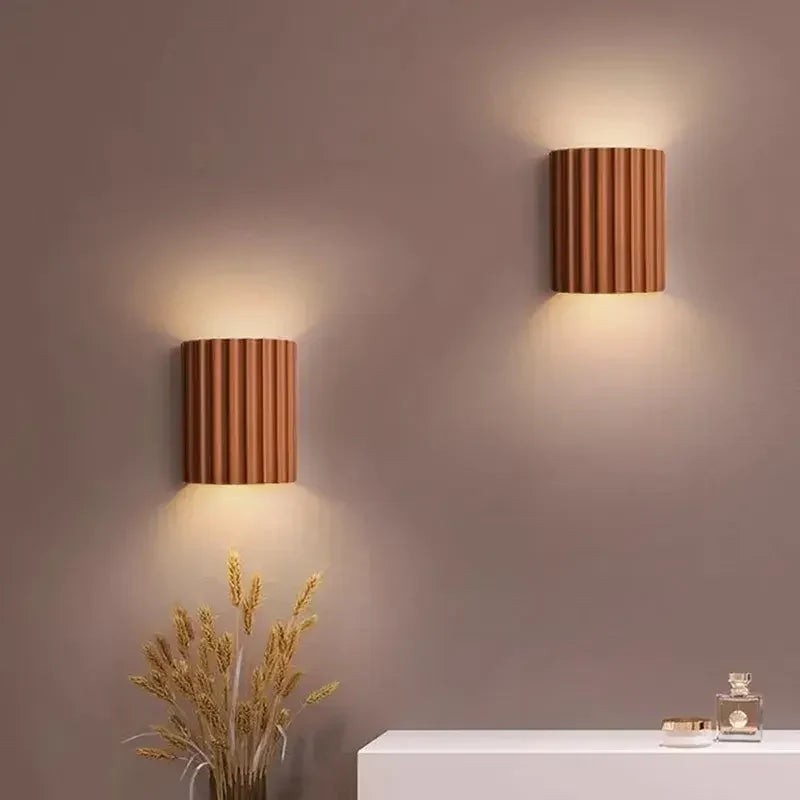 Zwei terrakottafarbene gerillte Wandlampen leuchten an einer Wand über Trockengräsern und einem weißen Regal 8