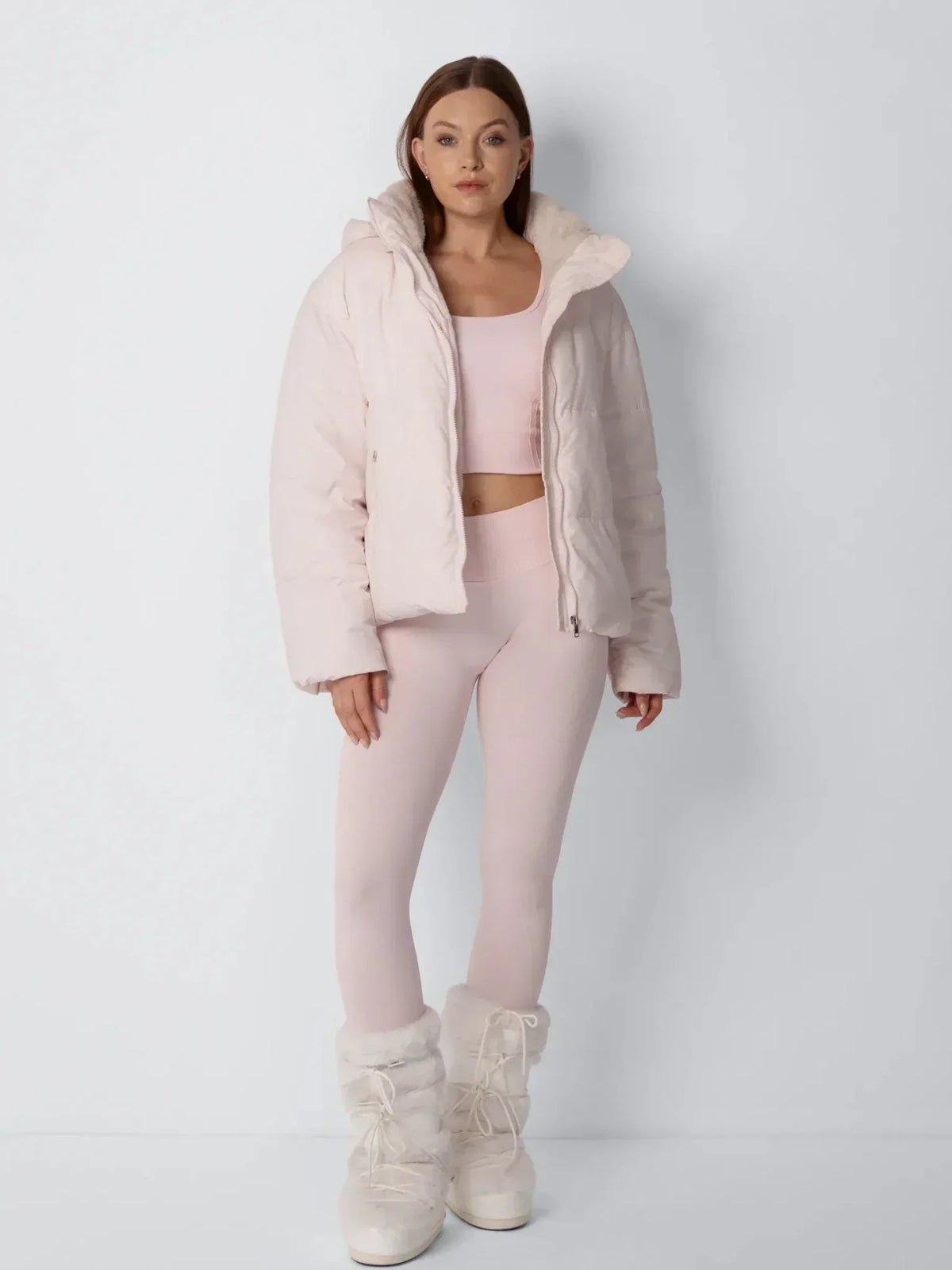 Ganzkörperfoto des Models in offener rosa Steppjacke mit rosa Set und weißen Fellstiefeln 10