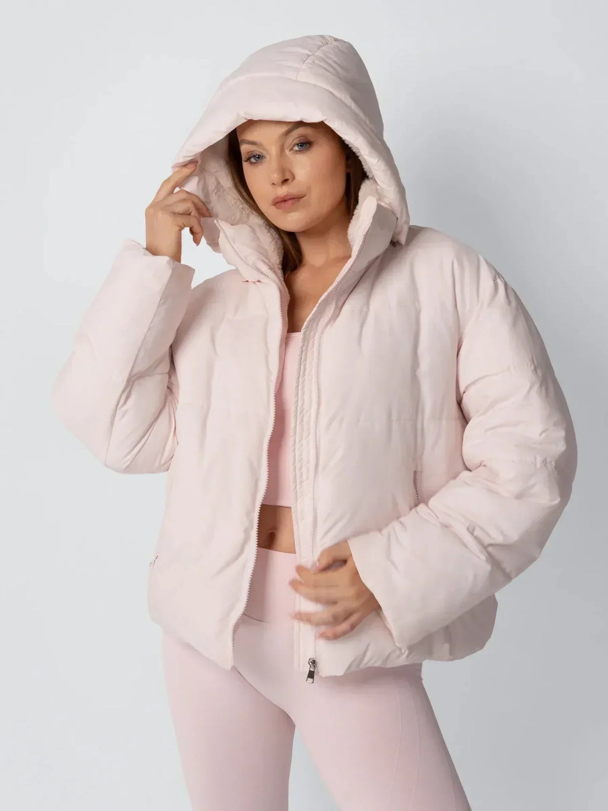 Model in rosafarbener Steppjacke mit aufgesetzter Kapuze und Fleecefutter, Hand am Kapuzenrand 6