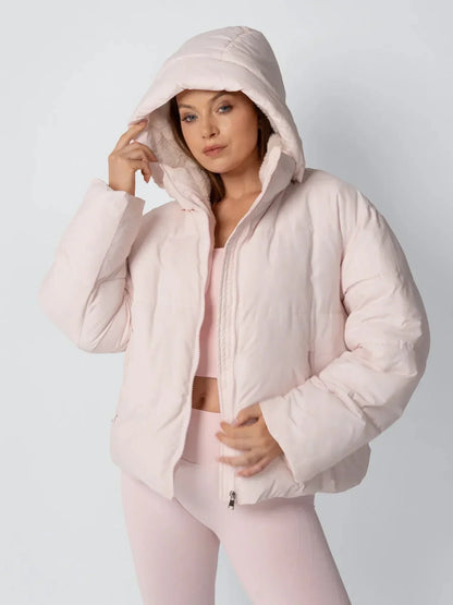 Model in rosafarbener Steppjacke mit aufgesetzter Kapuze und Fleecefutter, Hand am Kapuzenrand 6