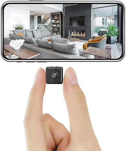 Winzige schwarze Würfelkamera zwischen zwei Fingern gehalten, darüber ein Smartphone mit Live-Bild eines Wohnzimmers mit Sofa und Kamin. 1