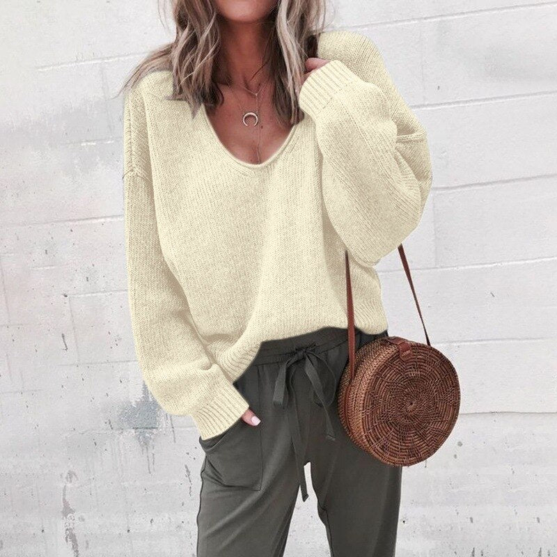 Frau in cremefarbenem V-Ausschnitt Strickpullover, grüne Hose, runde Strohtasche.