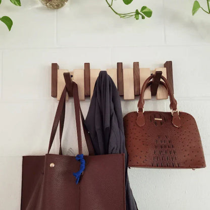 Helle Holzgarderobe mit dunklen Haken an weißer Wand, daran hängen zwei braune Taschen und eine Jacke 2