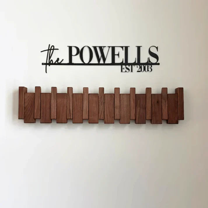 Dunkle Holzgarderobe mit eingeklappten Haken, an der Wand unter einem schwarzen Metallschriftzug montiert 5