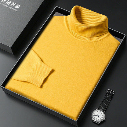 Gelber Rollkragenpullover gefaltet in einer schwarzen Box, daneben eine Armbanduhr mit hellem Zifferblatt und Lederarmband; die Geschenkverpackung steht links d