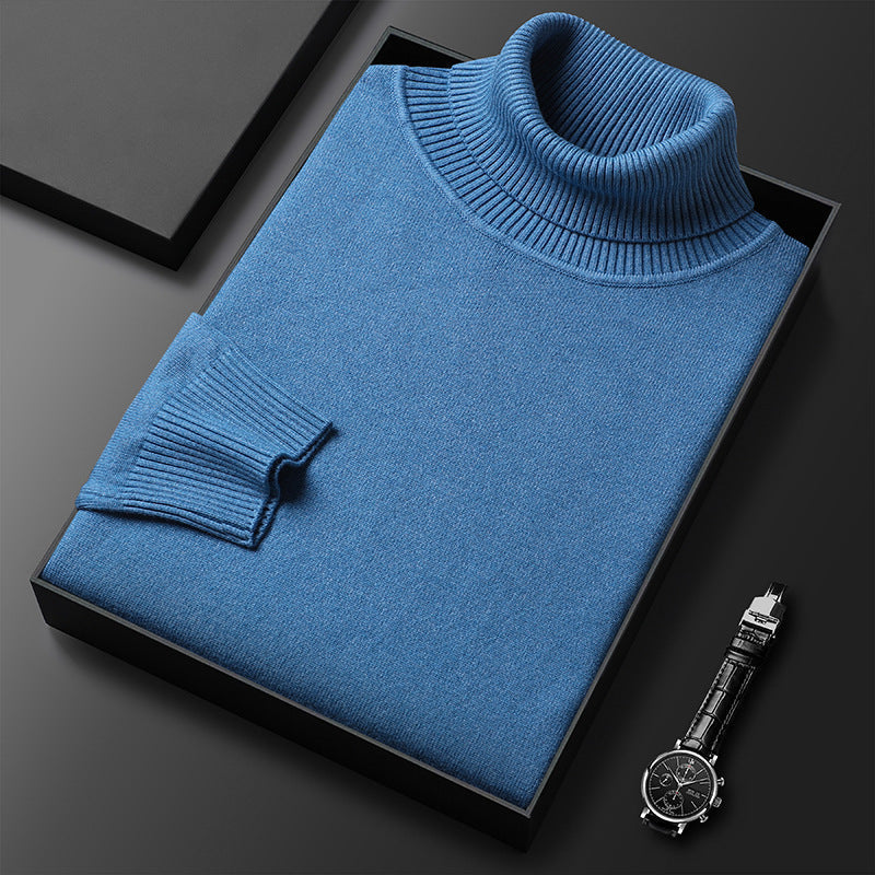 Blauer Rollkragenpullover gefaltet in einer schwarzen Box, daneben eine Armbanduhr mit Lederarmband; Rippkragen und Rippbündchen am Ärmel sichtbar. 2