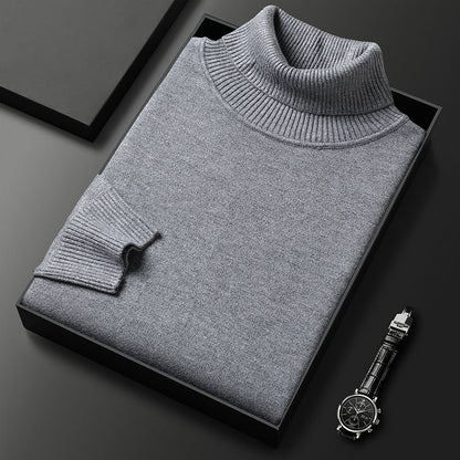 Grauer Rollkragenpullover gefaltet in einer schwarzen Box, daneben eine Armbanduhr mit Lederarmband; Rippkragen und Rippbündchen am Ärmel sichtbar. 5