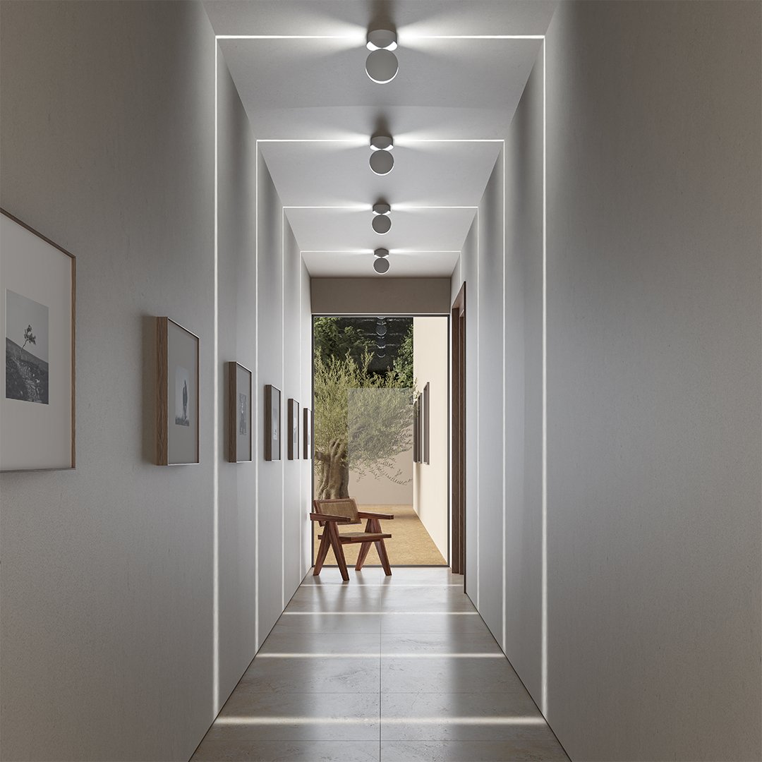 Flur mit vier weißen Deckenleuchten, deren Licht rechteckige Lichtrahmen an Wänden, Decke und Boden zeichnet, im Hintergrund ein Holzstuhl. 1