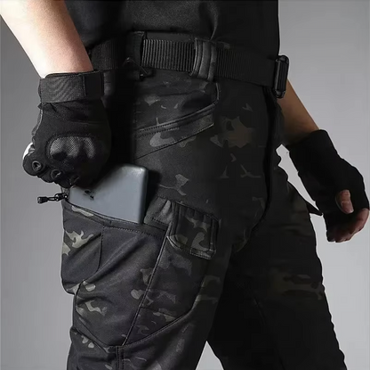 Detail der Camouflage-Hose am Model mit Gürtel, Handschuhen und Smartphone in der seitlichen Reißverschlusstasche am Oberschenkel.